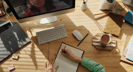 A picture of someone writing notes in a notebook while talking to a colleague via a video chat