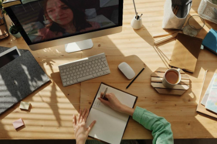 A picture of someone writing notes in a notebook while talking to a colleague via a video chat